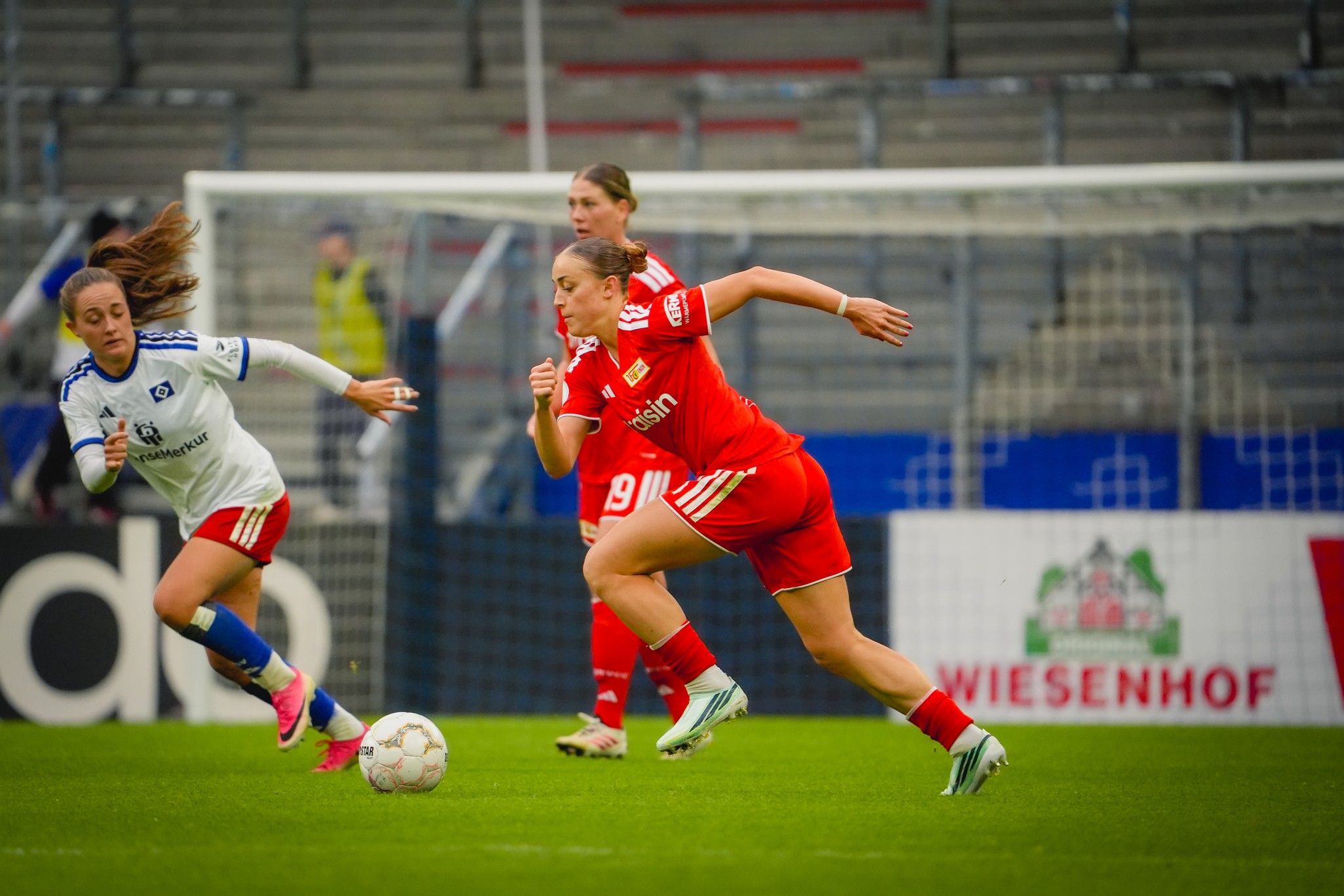 Eine Spielerin in roter Kleidung sprintet mit dem Ball, während eine gegnerische Spielerin in Weiß hinterherläuft.