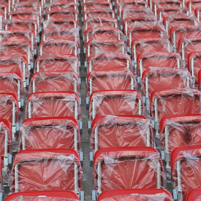 Reihe von roten Stadionstühlen, die in Plastikfolie verpackt sind, in gleichmäßigen Abständen angeordnet.