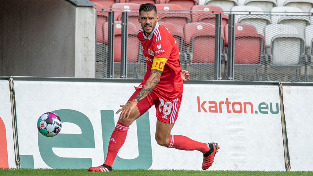 A football player in a red jersey with a captain's armband is taking a throw-in.