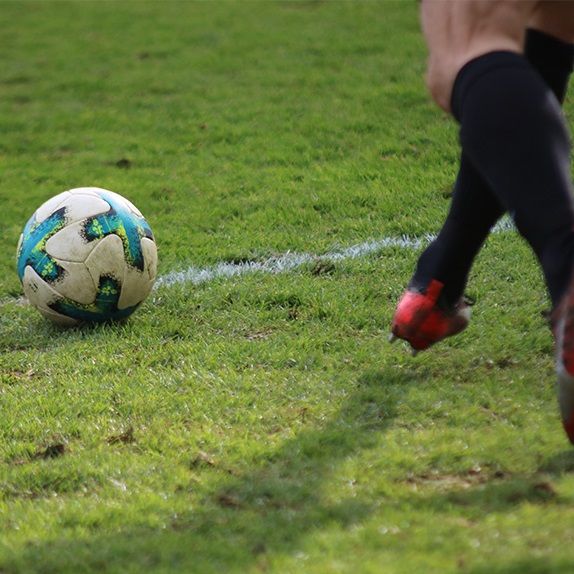 Ein Fußball liegt auf einem grünen Rasenfeld, während ein Spieler sich ihm nähert.