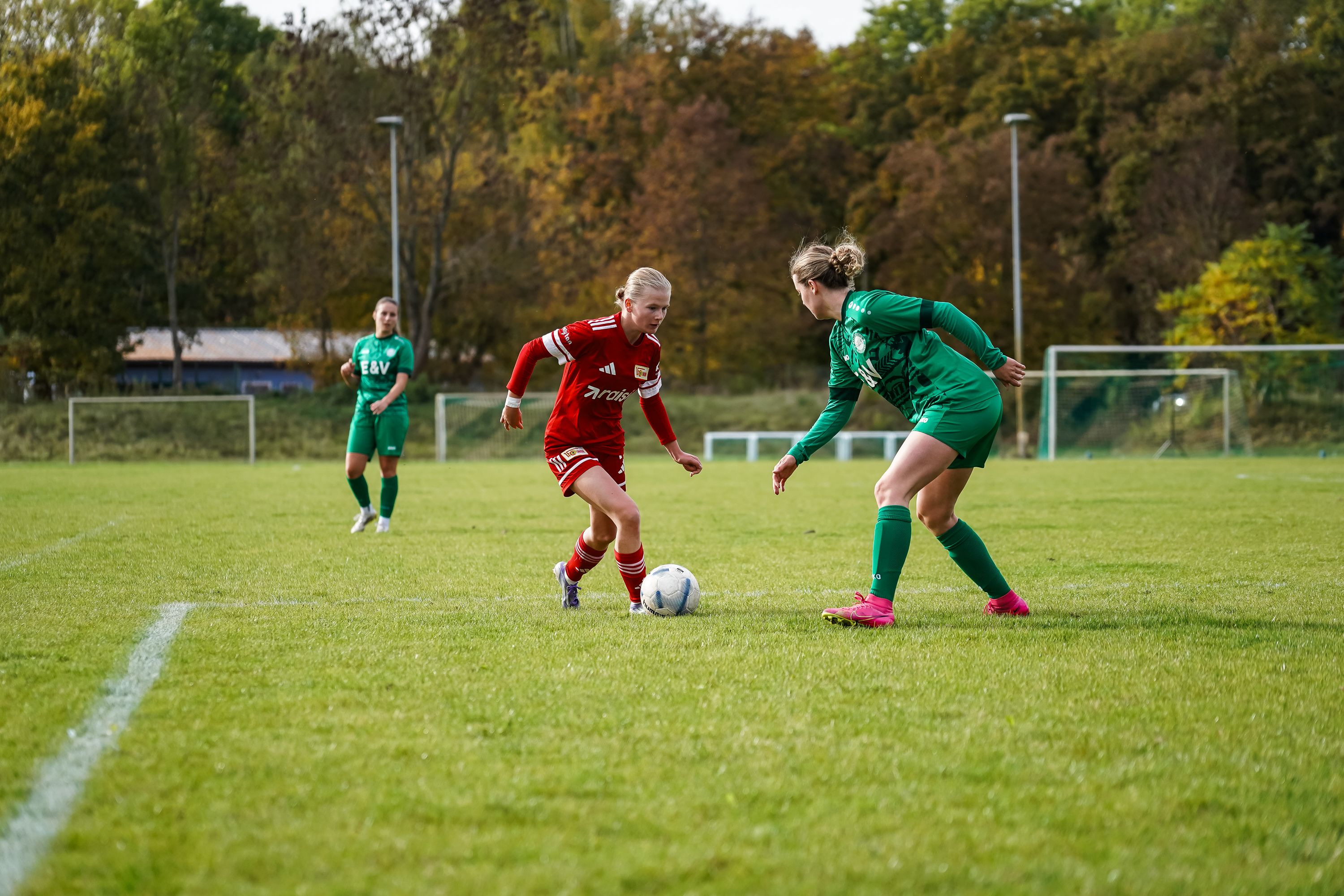 Zwei Fußballspielerinnen im Wettkampf um den Ball auf einem Rasenplatz in einem Herbstsetting.