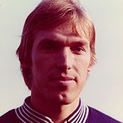 Porträt eines Mannes mit blonden Haaren, der in einem sportlichen Polohemd mit Streifen am Kragen lächelt.