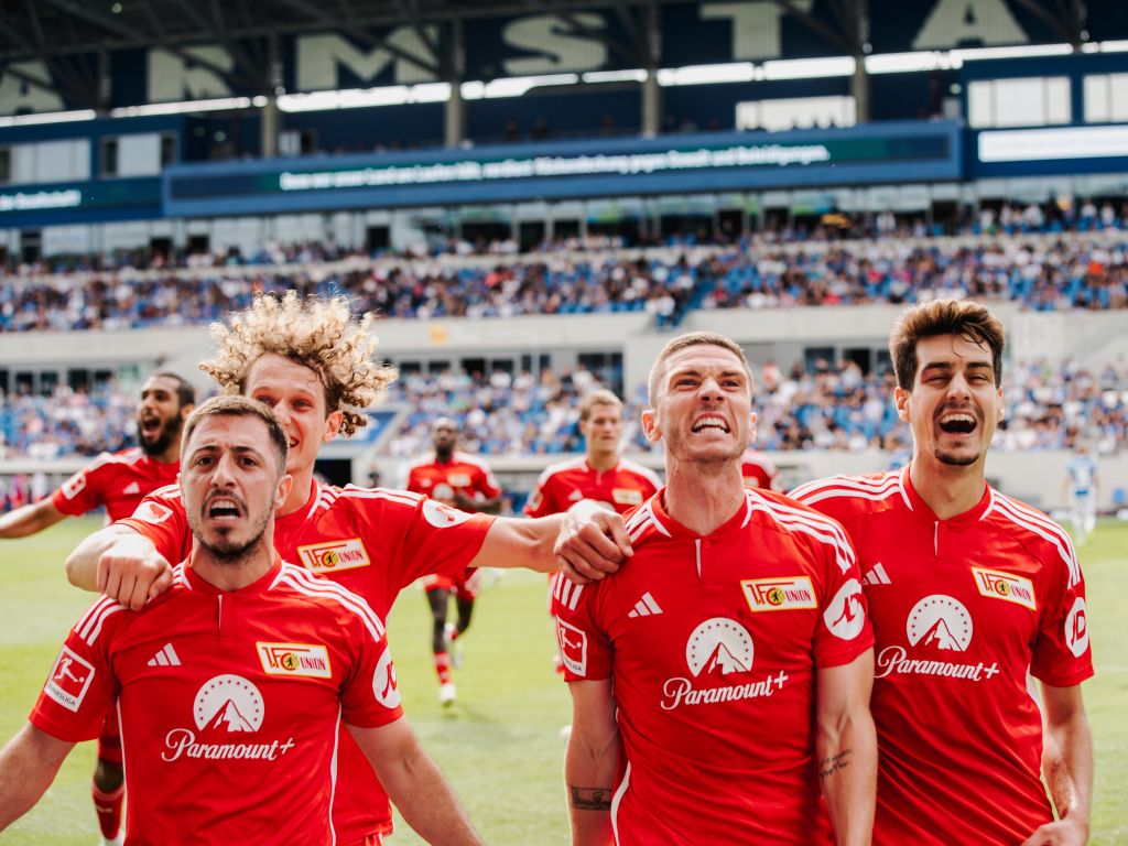 Eine Gruppe von Spielern trägt rote Trikots. Sie freuen sich auf dem Spielfeld. Die Zuschauer jubeln.