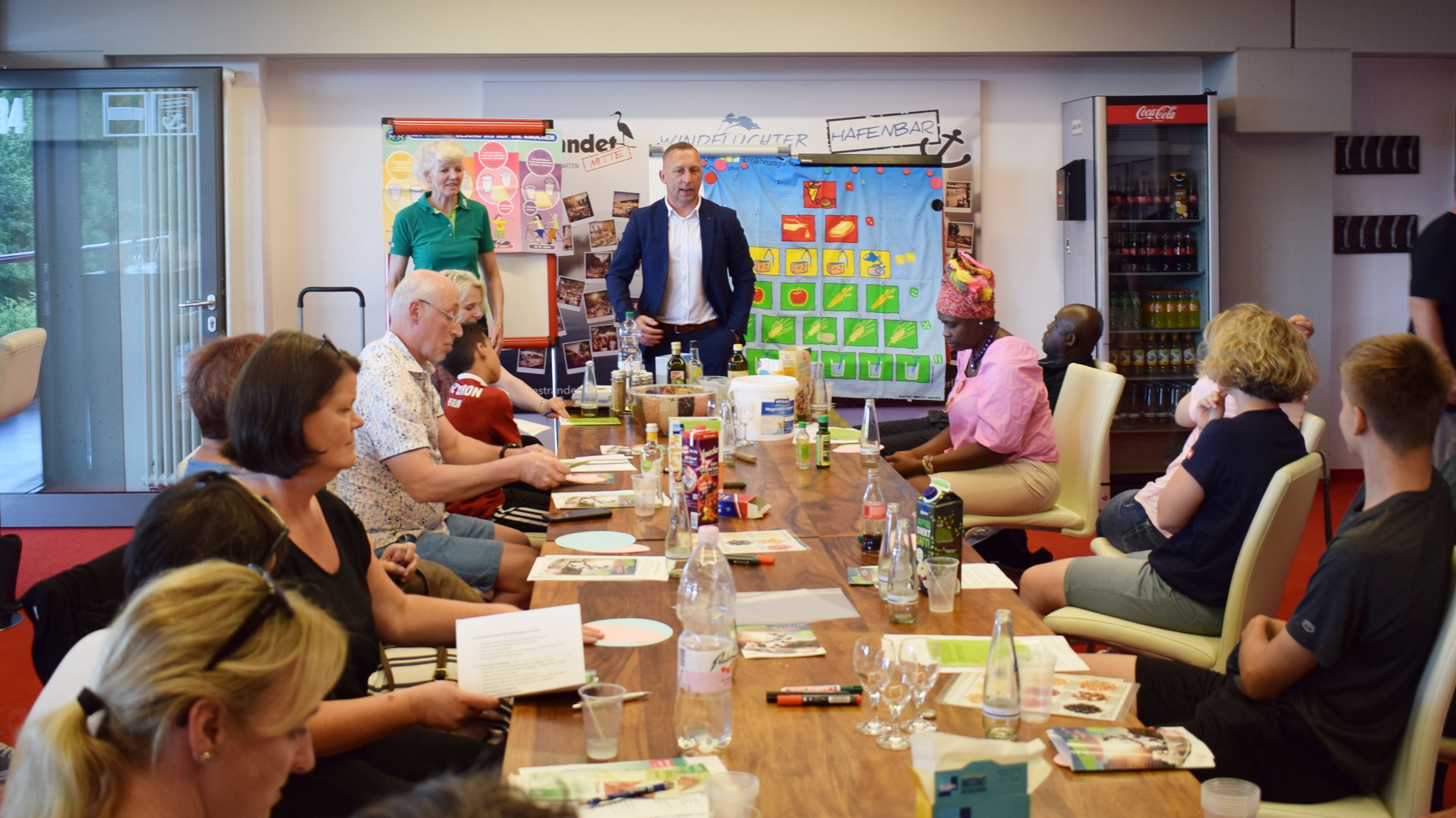 Eine Gruppe von Menschen sitzt an einem Tisch in einem Konferenzraum, während eine Person vorne spricht und eine Präsentation zeigt.