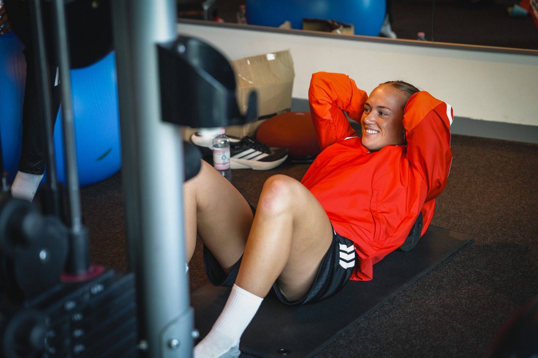 Eine Person in einem roten Sportoberteil macht Crunches auf einer Matte im Fitnessstudio.