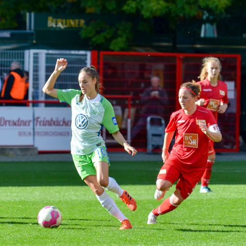 Zwei Fußballspielerinnen auf dem Spielfeld, eine in grünem Trikot, die andere in rotem Trikot, während eines Spiels in Aktion.