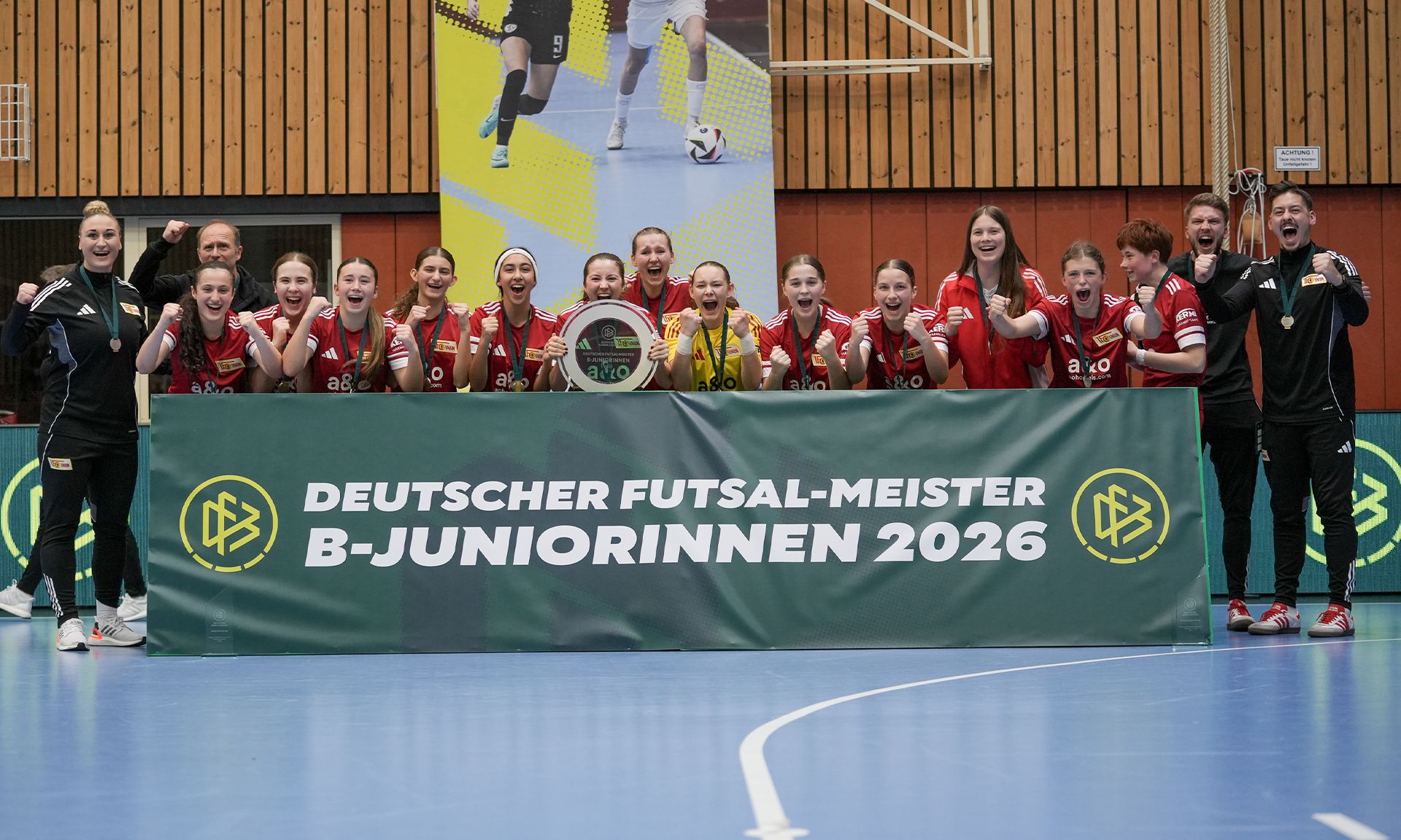 Junge Frauen in roten Trikots posieren mit Pokal und freuen sich über den Titel "Deutscher Futsal-Meister B-Juniorinnen 2026".