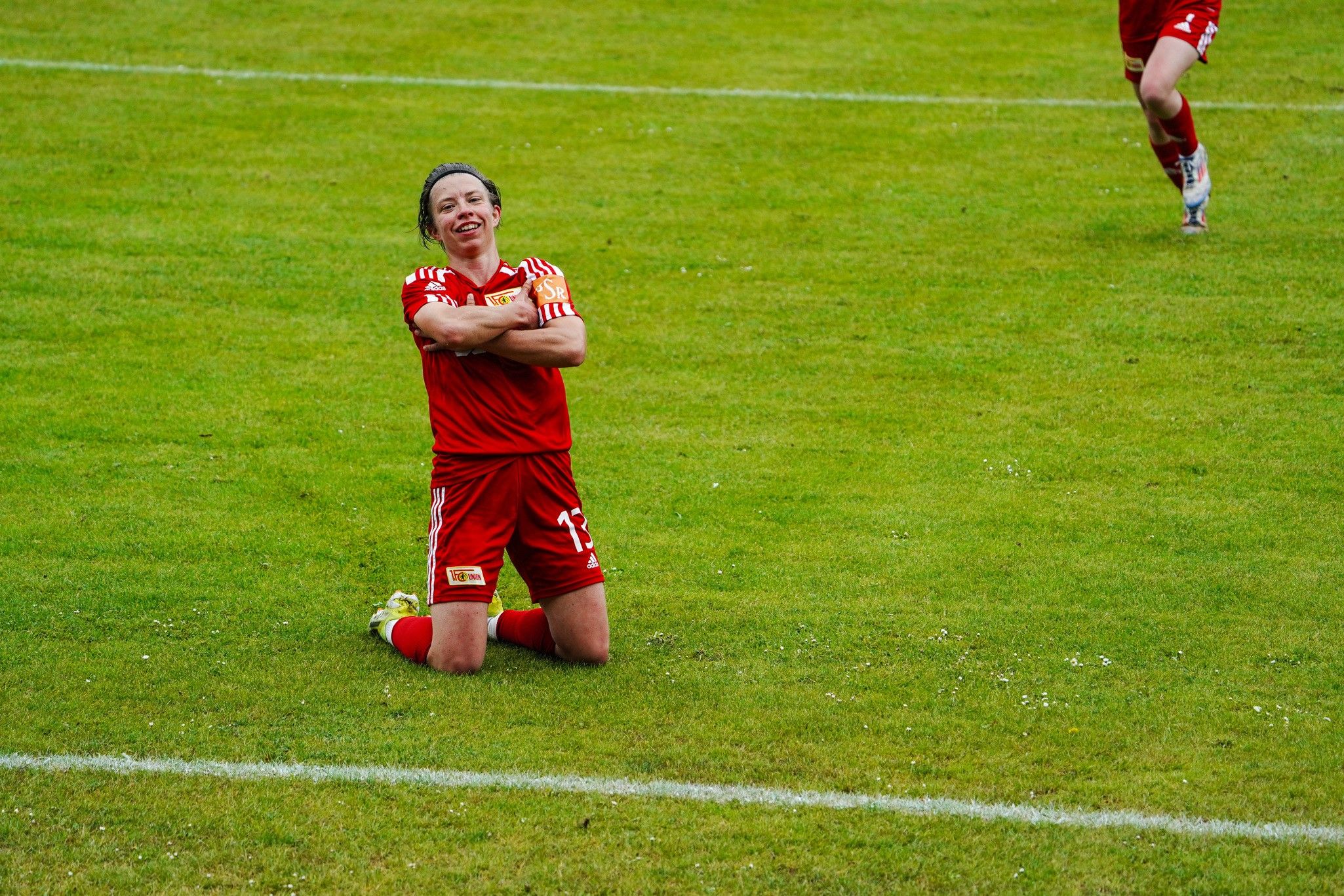 Eine Fußballspielerin in rotem Trikot kniet jubelnd auf dem Rasen nach einem Tor.
