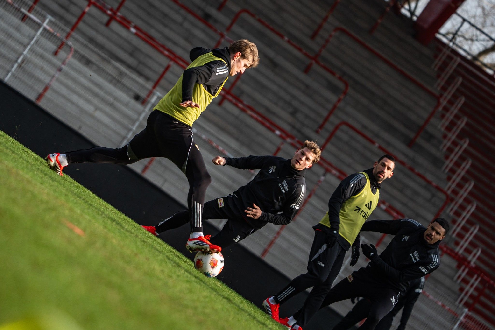 Fußballtraining mit mehreren Spielern, die ein Passspiel auf einem Rasenfeld üben. Zuschauertribüne im Hintergrund.