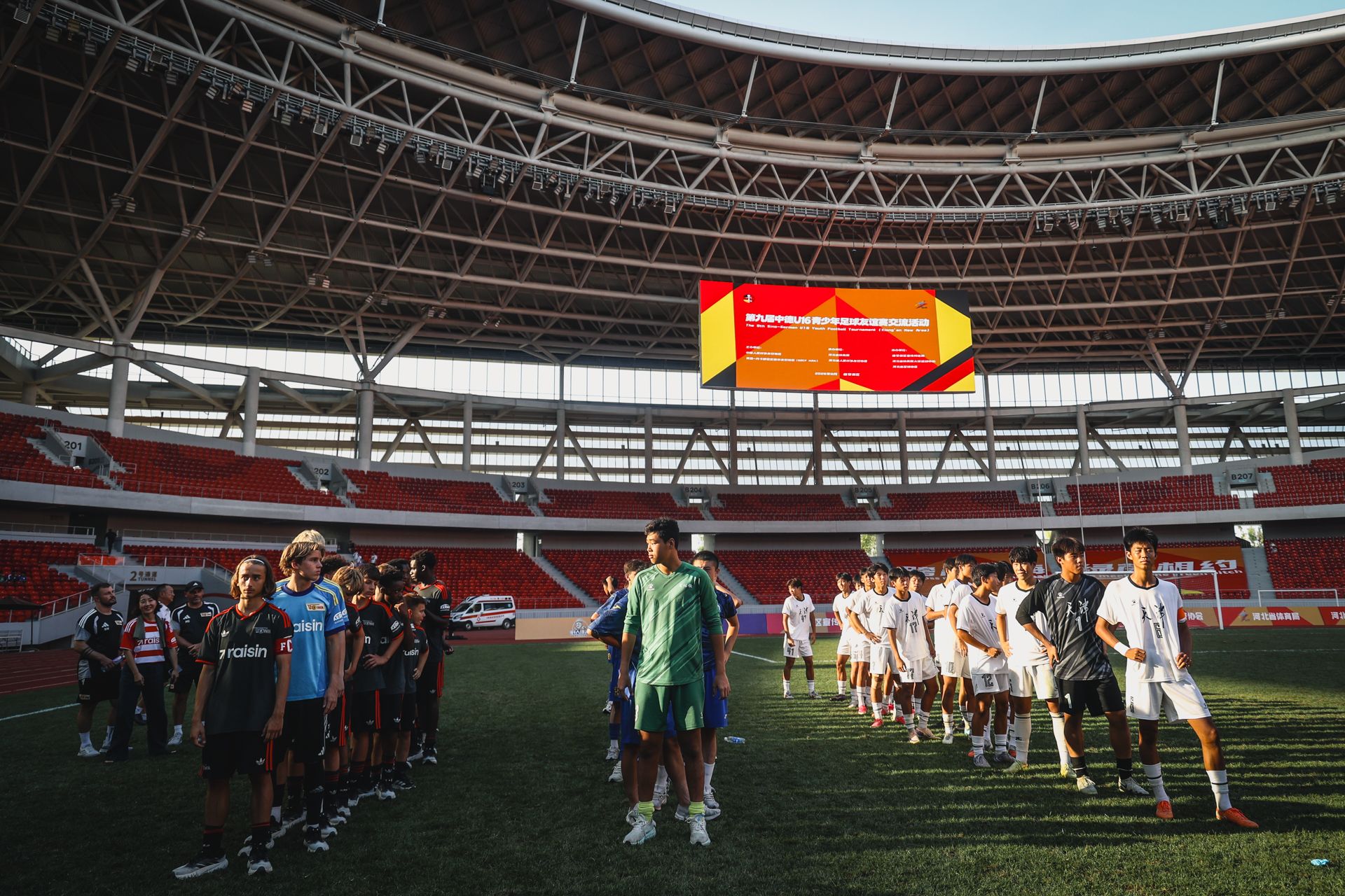 Zwei Fußballmannschaften stehen auf dem Spielfeld und bereiten sich auf das Spiel vor, im Hintergrund ein großes Stadionbanner.