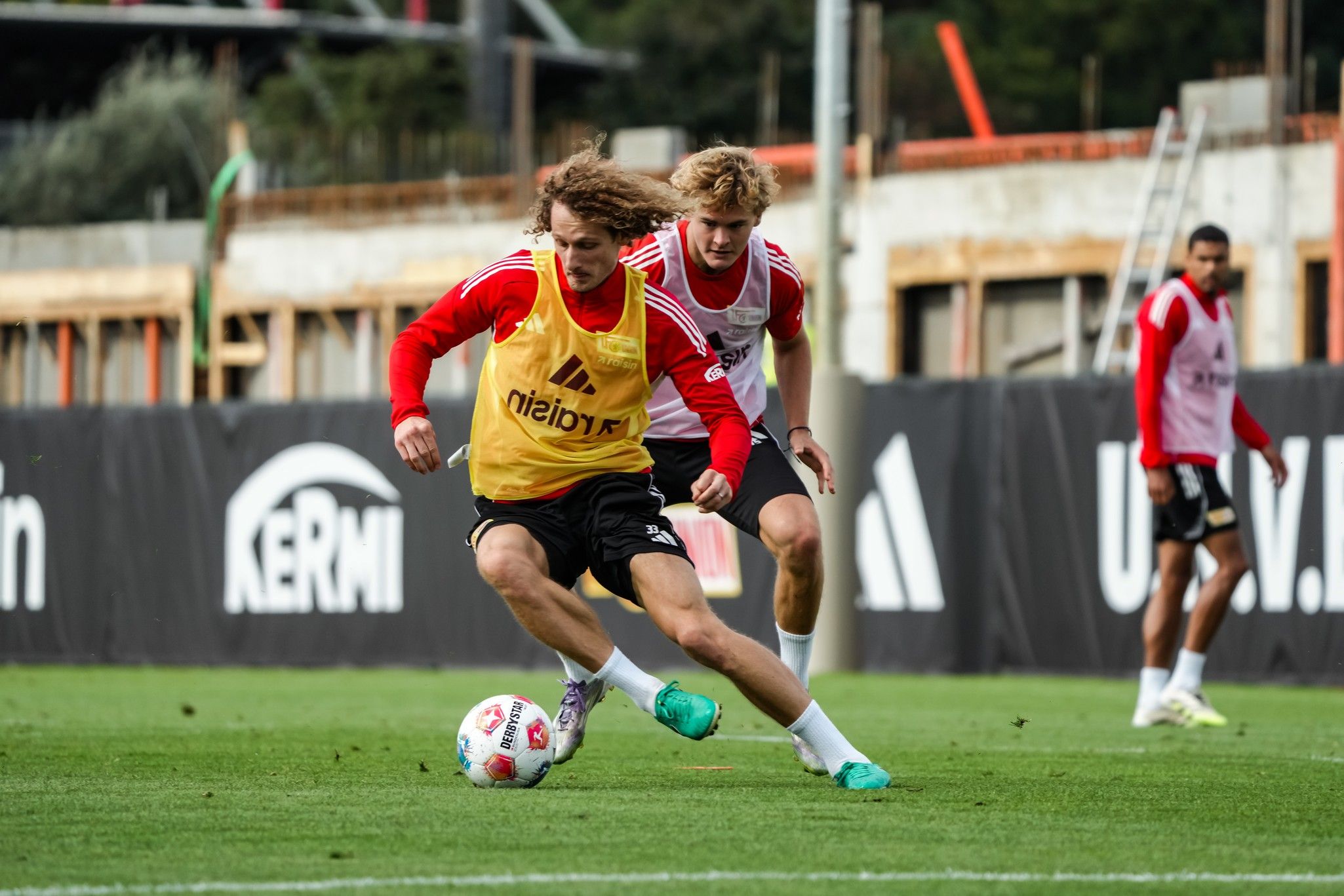 Zwei Fußballspieler im Training, einer mit gelbem Trikot dribbelt den Ball, während der andere verfolgt.