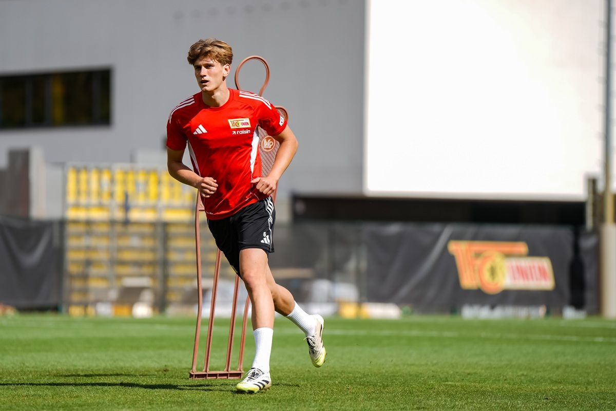 Ein junger Fußballspieler in rotem Trikot joggt auf einem Trainingsplatz, umgeben von Markierungsstäben.