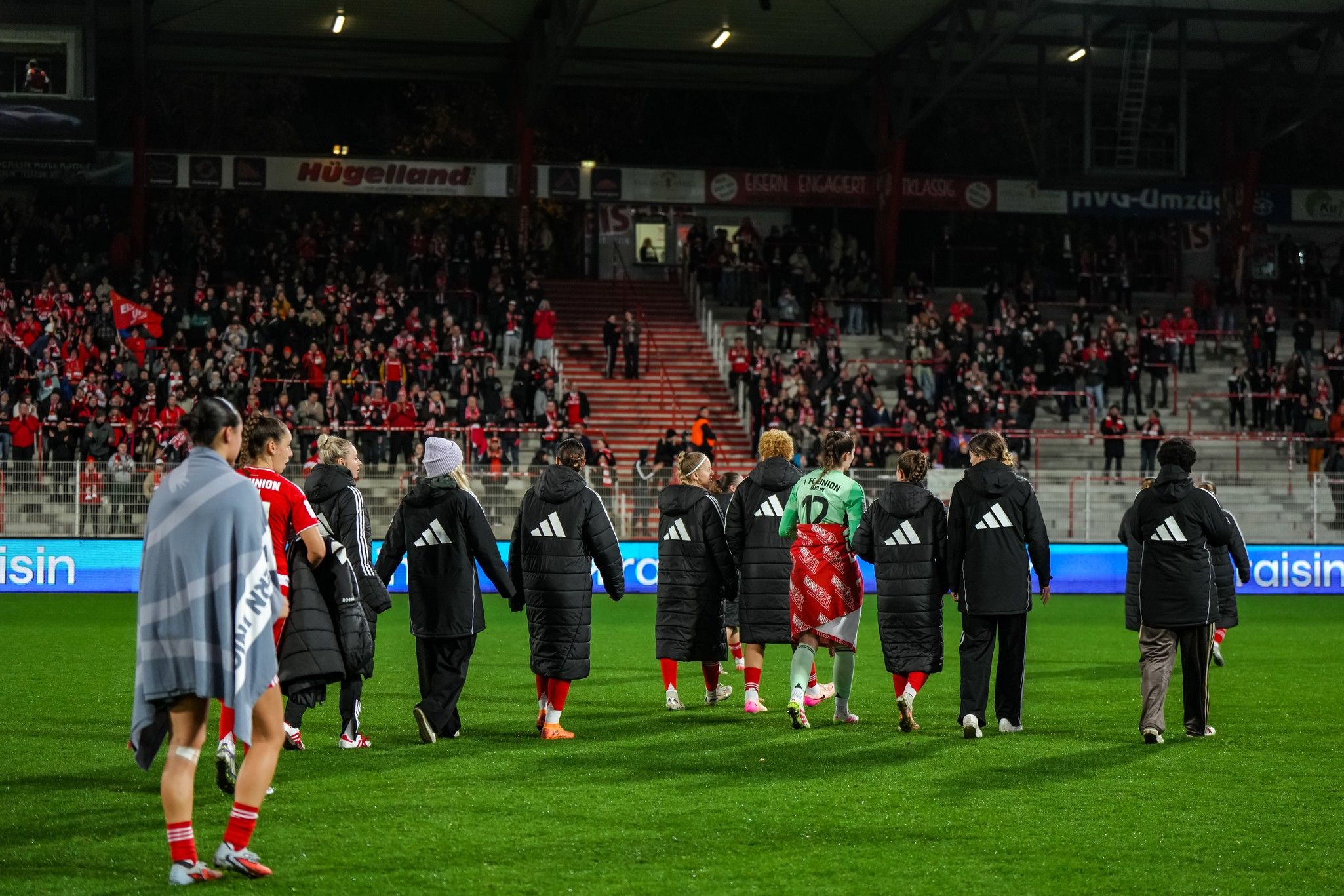 Spieler gehen auf das Spielfeld, um ihre Fans zu begrüßen, während im Hintergrund eine jubelnde Menge zu sehen ist.