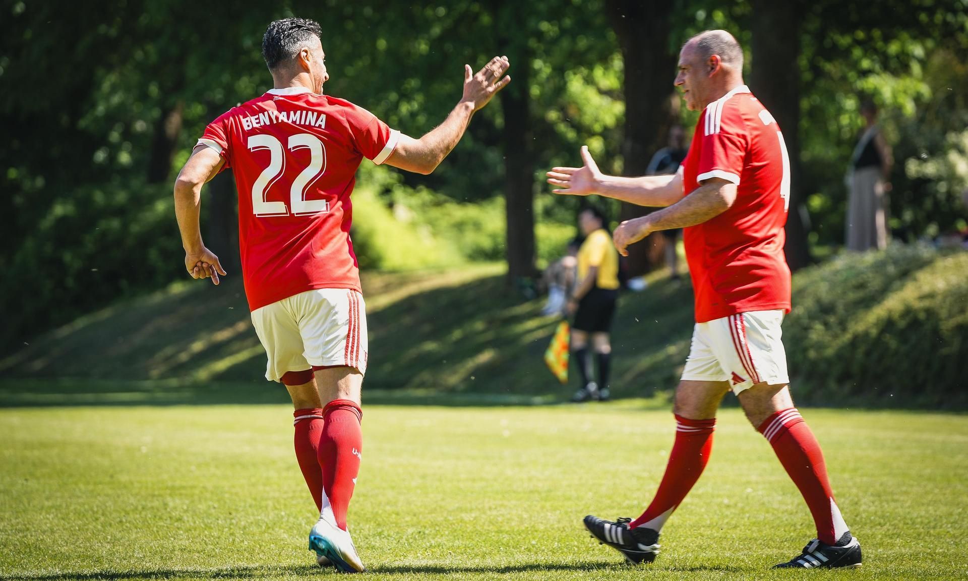 Zwei Fußballspieler in roten Trikots mit der Nummer 22, die sich nach einem Spielzug begrüßen. Im Hintergrund ist ein grünes Feld.