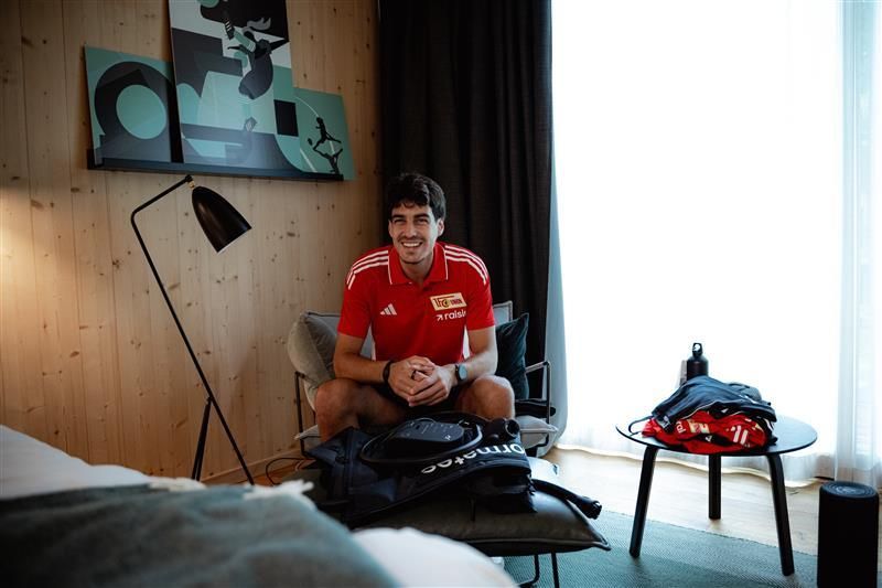 Ein Sportler sitzt in einem Hotelzimmer auf einem Sessel, umgeben von Ausrüstung und persönlichem Gepäck.