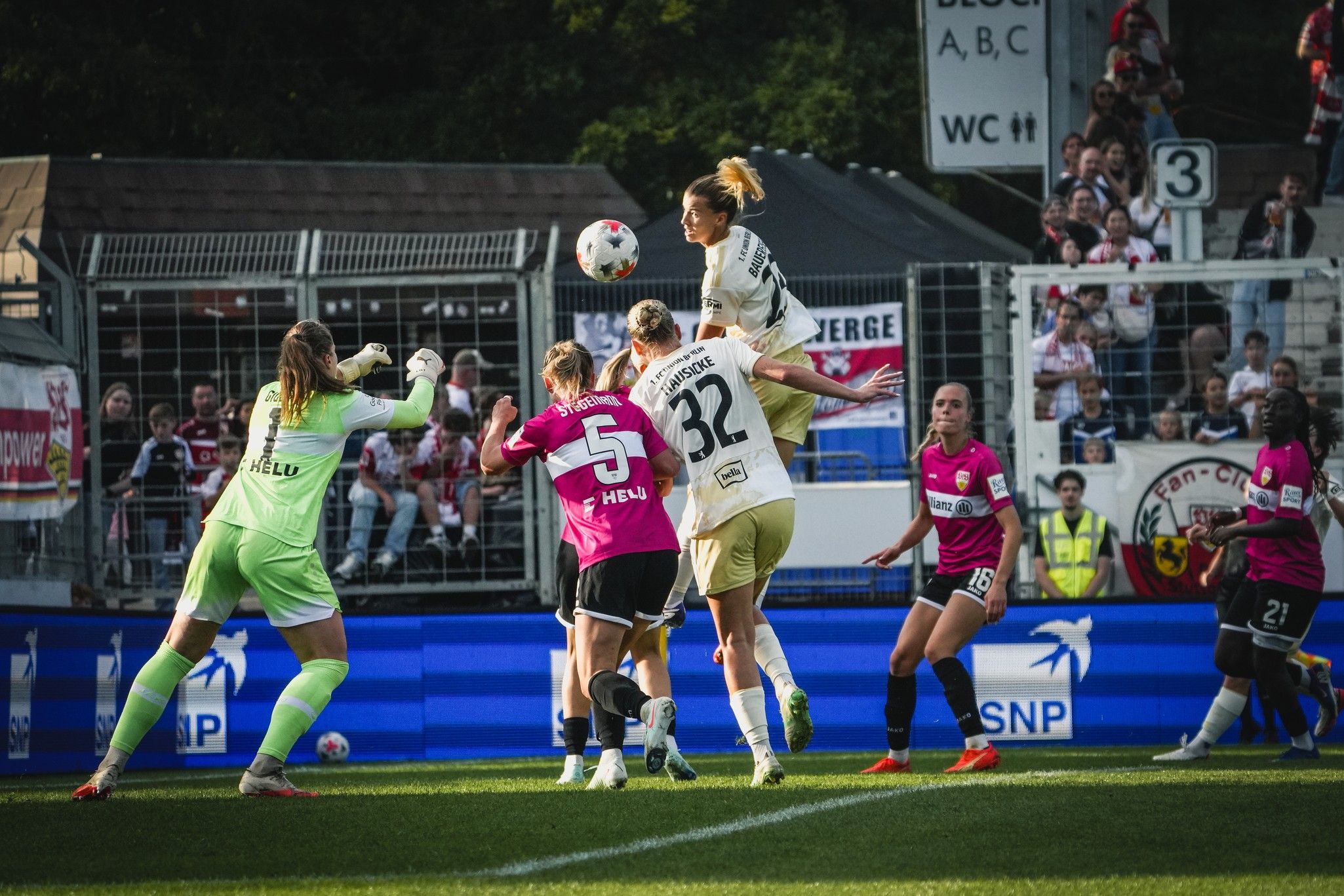 Eine Spielerin springt hoch, um den Ball während eines Fußballspiels zu köpfen, während die Torhüterin und andere Spielerinnen anwesend sind.