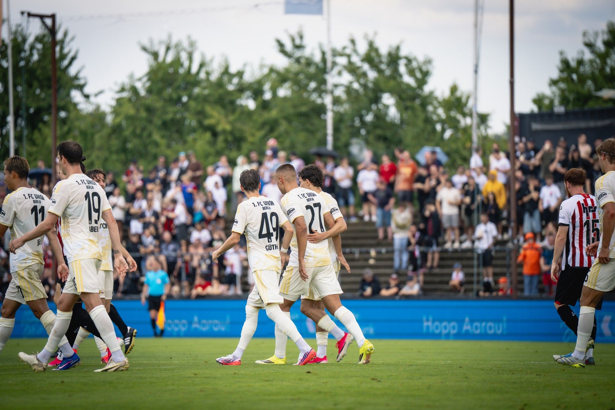 Fußballspieler in einheitlichen Trikots laufen auf dem Spielfeld, während Zuschauer im Hintergrund zuschauen.