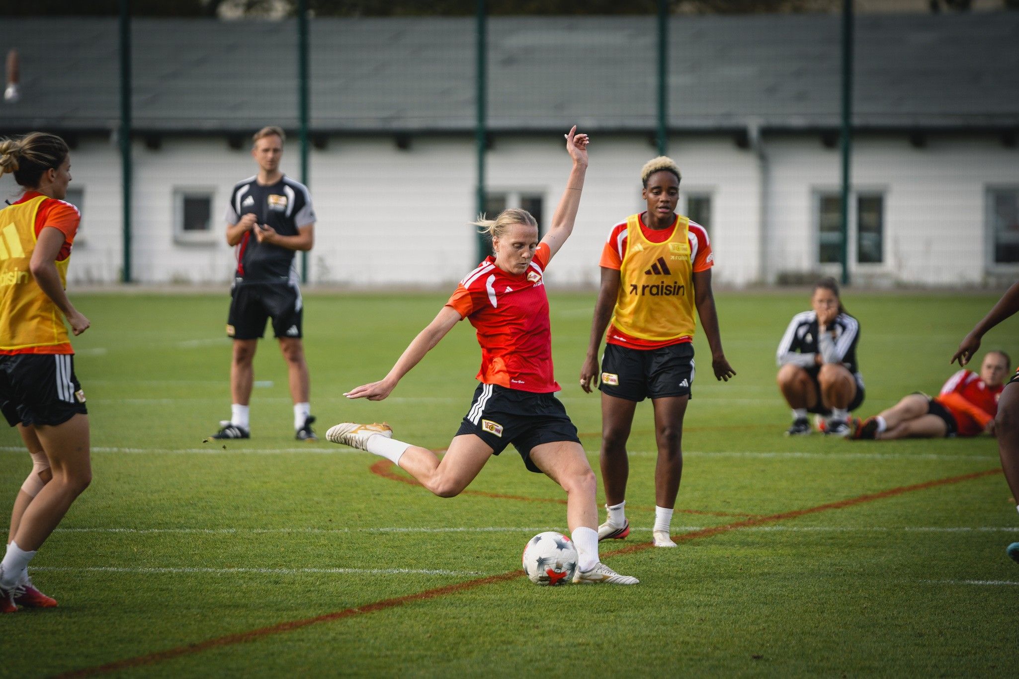 Eine Fußballspielerin schießt den Ball während des Trainings, umgeben von weiteren Spielerinnen auf einem grünen Rasenplatz.