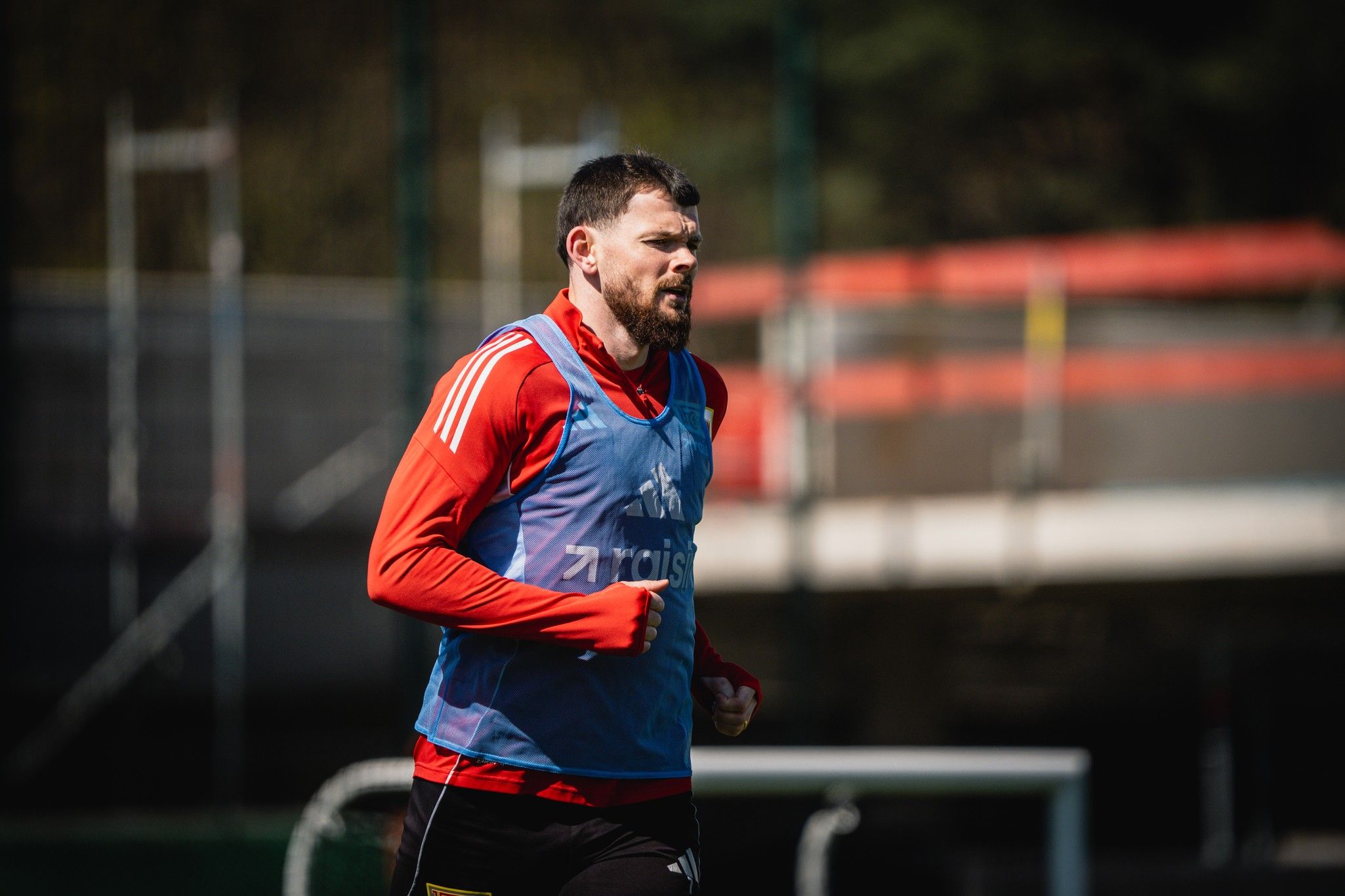 Ein mit einem Trainingsanzug bekleideter Fußballspieler joggt auf einem Sportplatz.
