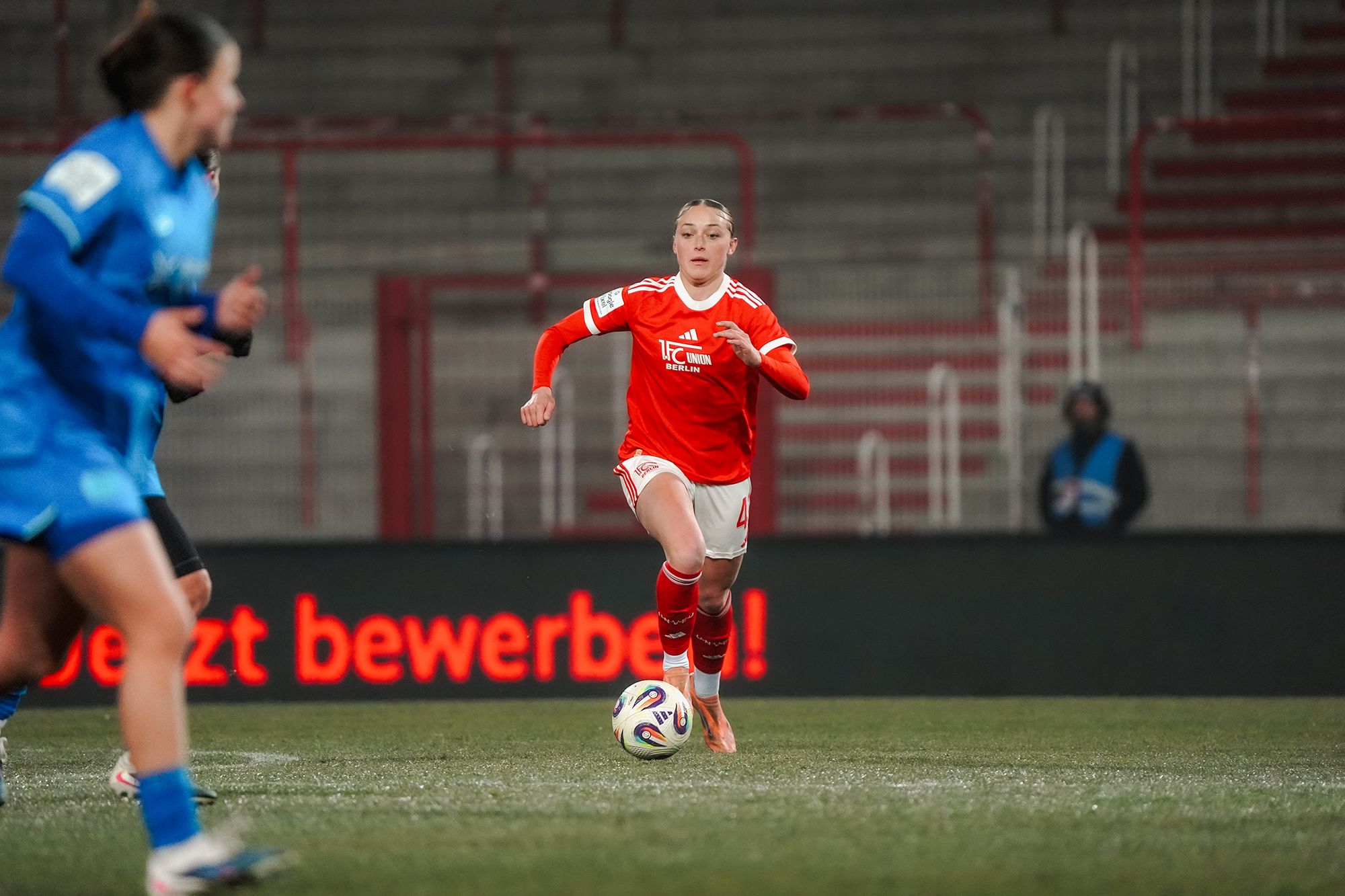 Eine Spielerin in rotem Trikot dribbelt den Ball auf dem Spielfeld während eines Fußballspiels.