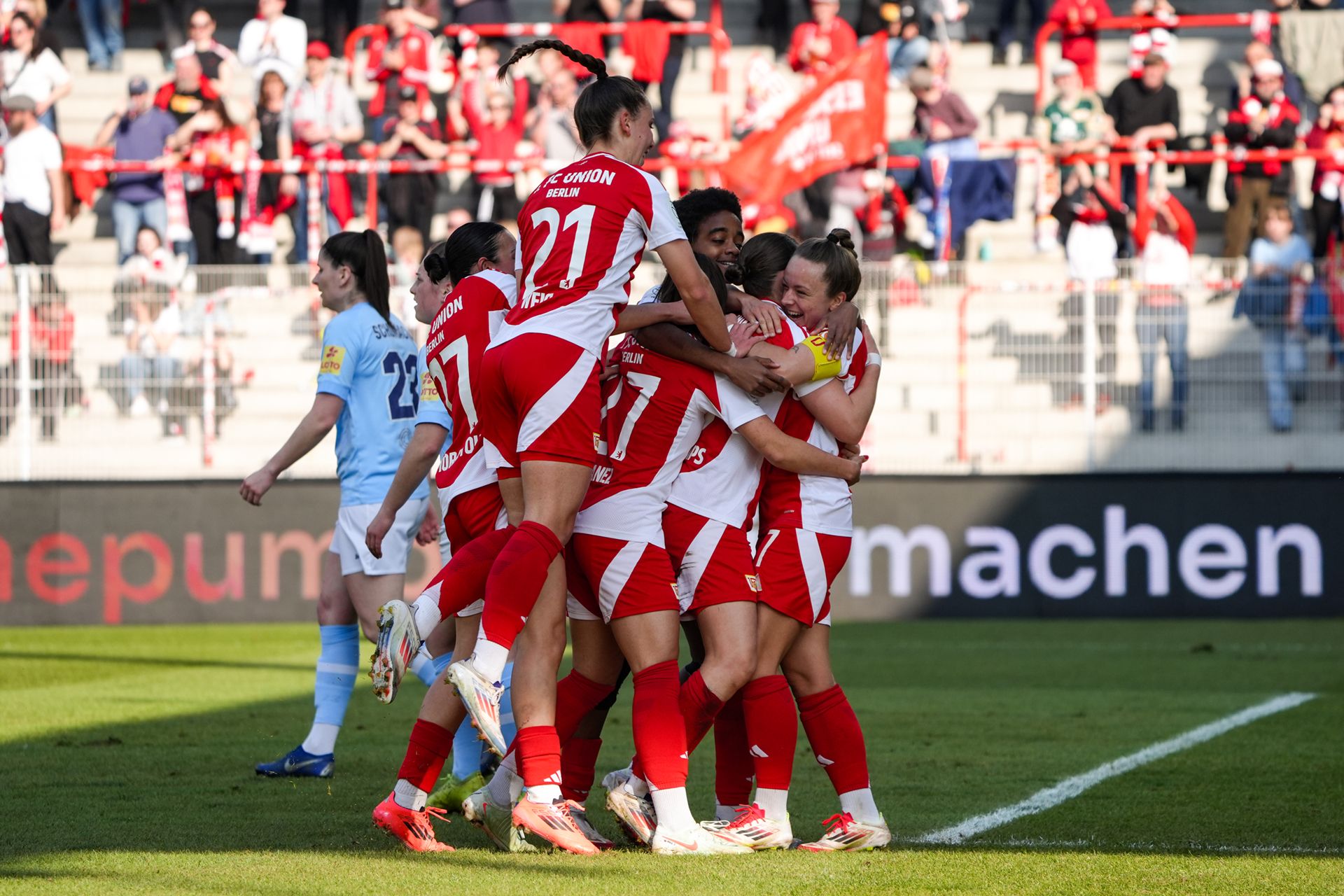 Spielerinnen eines Fußballteams feiern einen Torerfolg mit einem Sprung in einer jubelnden Gruppe auf dem Spielfeld.