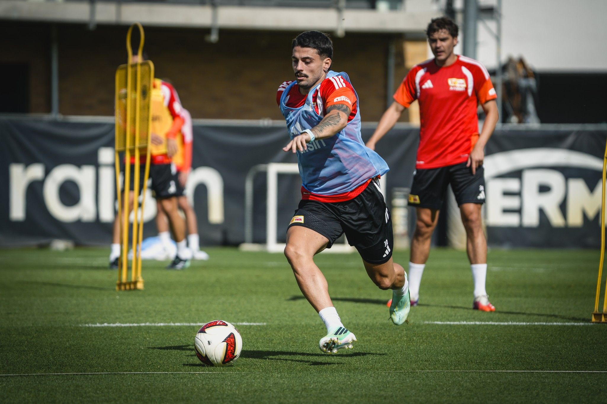 Ein Fußballspieler sprintet während des Trainings über den Platz, während andere Spieler im Hintergrund üben.