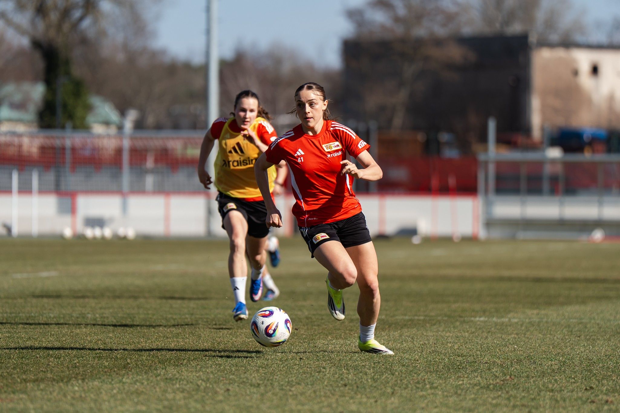 Eine Fußballspielerin in rotem Trikot sprintet mit Ball, während eine andere Spielerin im Hintergrund läuft.