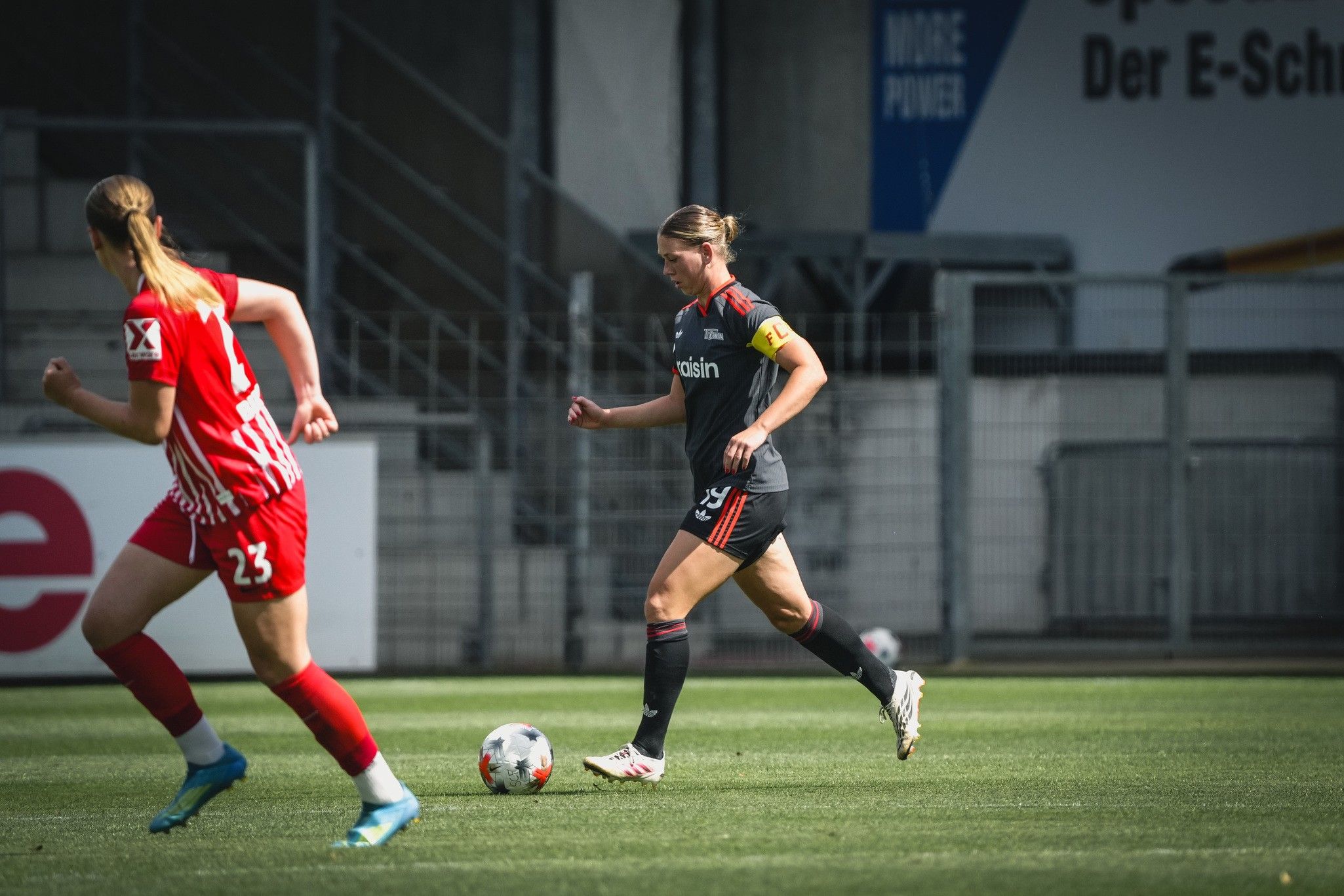 Eine Spielerin in einem schwarzen Trikot mit der Nummer 10 dribbelt den Ball auf dem Feld, während eine gegnerische Spielerin in Rot zuschaut.