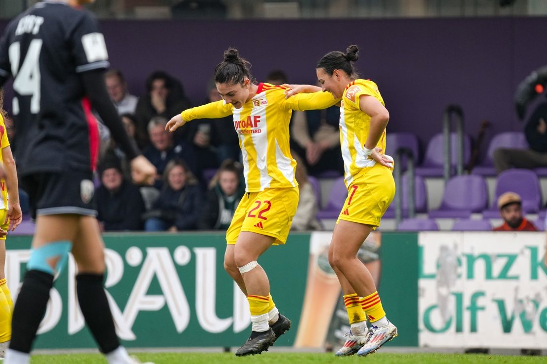 Zwei Spielerinnen des 1. FC Union feieren einen Torerfolg auf dem Spielfeld, umgeben von jubelnden Zuschauern.