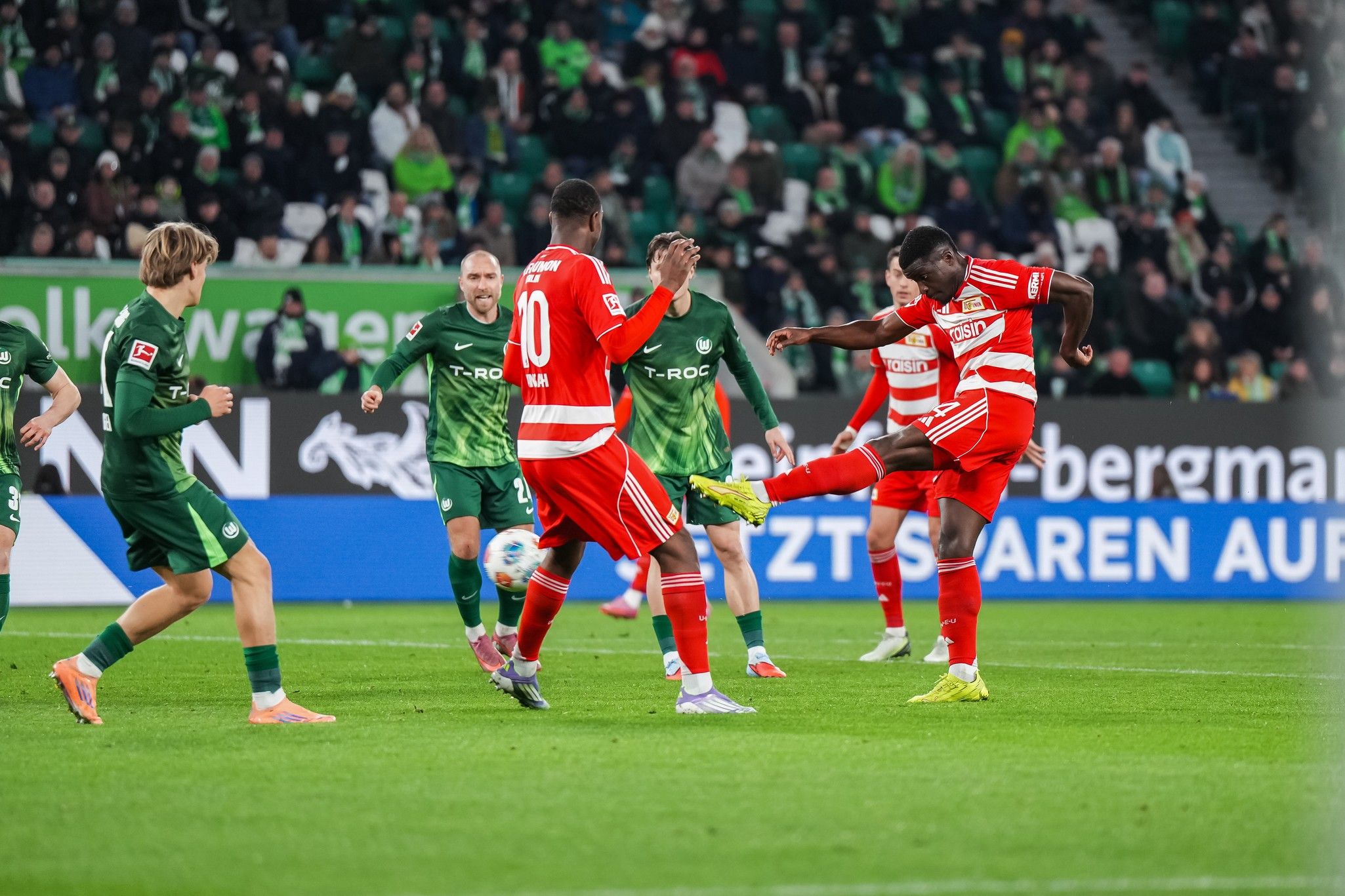 Spielszene aus einem Fußballspiel mit Spielern in roten und grünen Trikots, die um den Ball kämpfen.