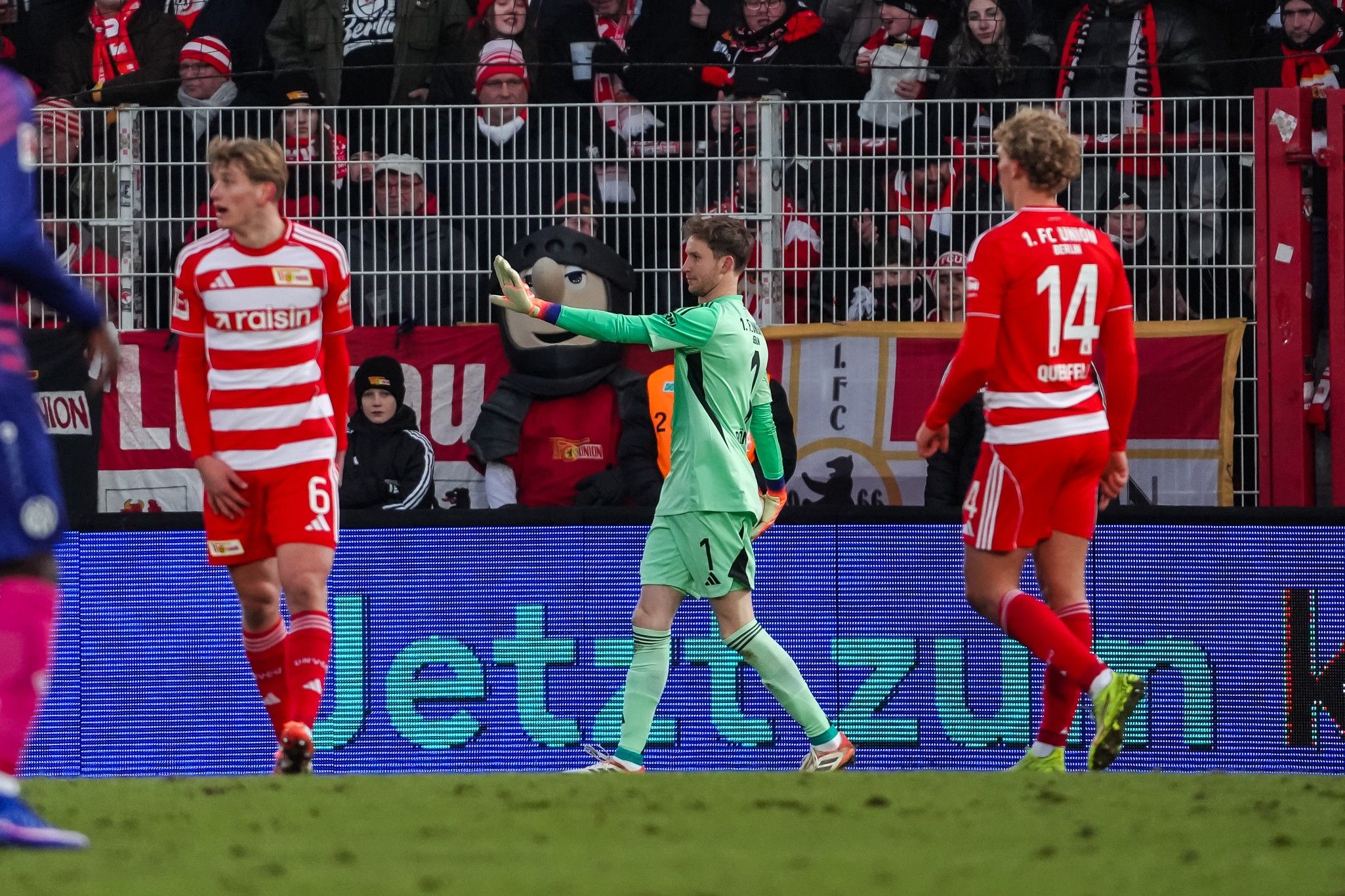 Fußballspieler in grüner Torwarttrikots mit Fans im Hintergrund, die vom Spielfeldrand jubeln.