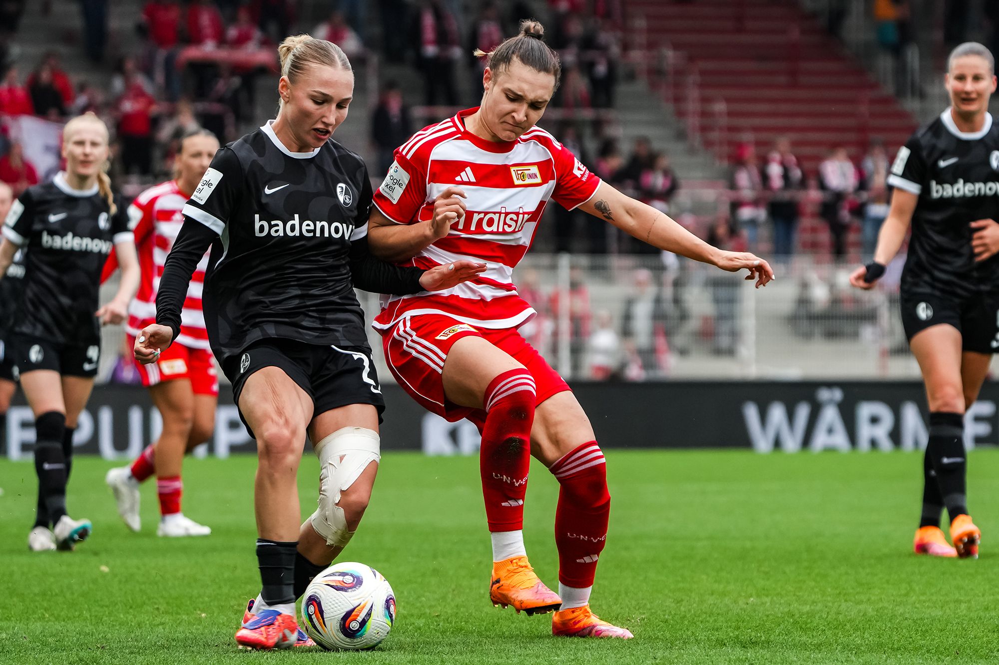 Zwei Frauenfußballspielerinnen im Wettbewerb um den Ball auf dem Spielfeld, eine in schwarzem und die andere in rotem Trikot.